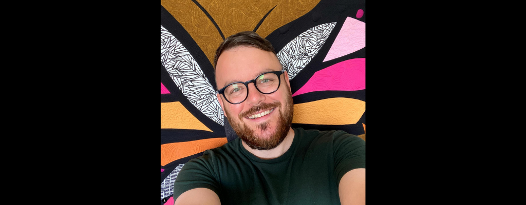picture of a white man with glasses and a beard against a colorful background